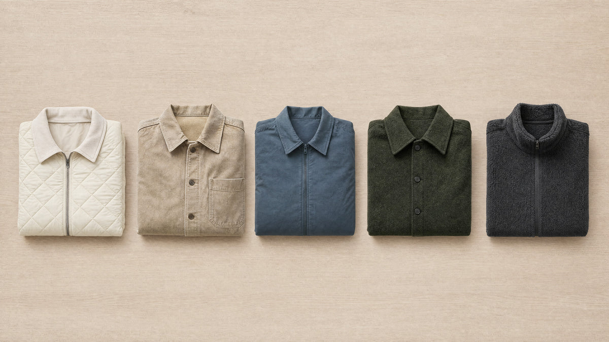 Five folded jackets laid out in a tonal row on pale oak